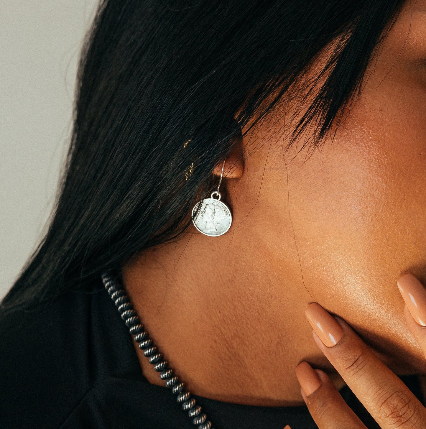 Woman wearing a black sleeveless top with decorative earrings and necklace.