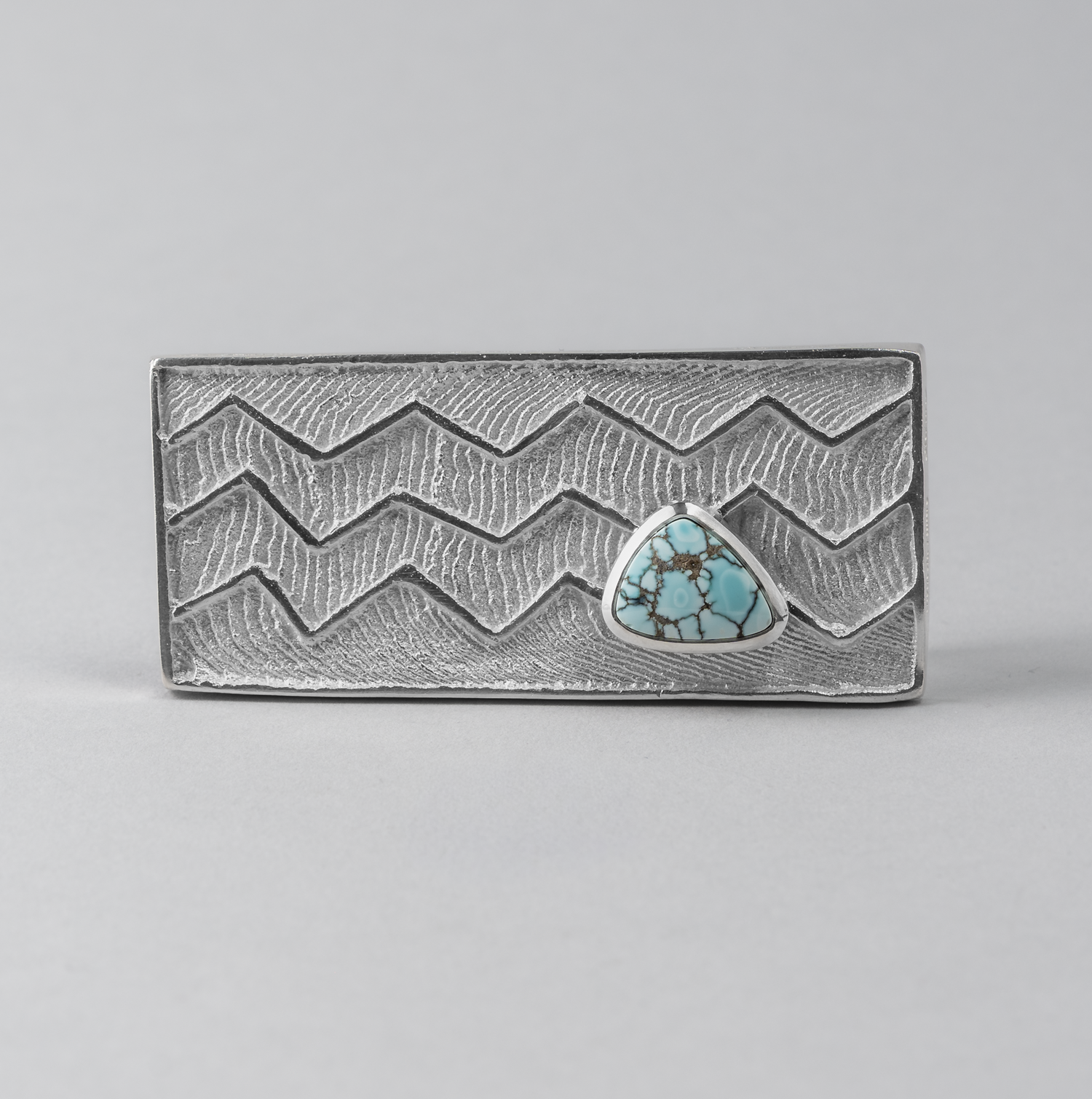 Silver belt buckle with a turquoise stone on a gray background
